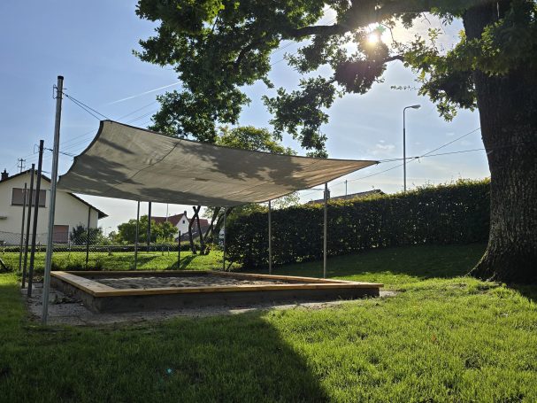 Sandkastenbeschattung Sonnenschutz über einem Sandkasten in einer Gartenlandschaft.